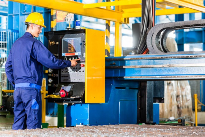 Worker in manufacturing plant at CNC machine control panel